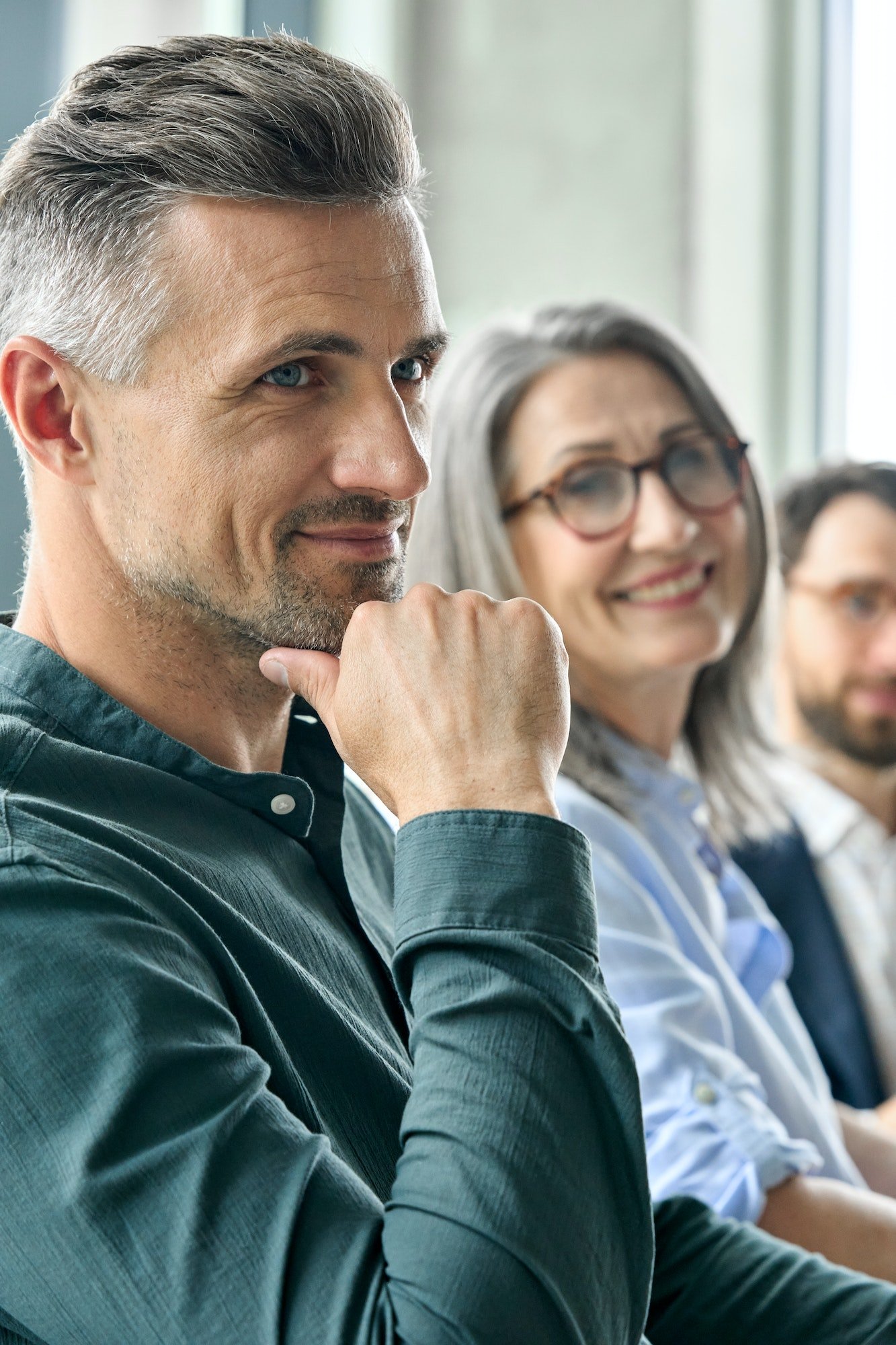 Smiling mature businessman sitting at office desk with executive team.