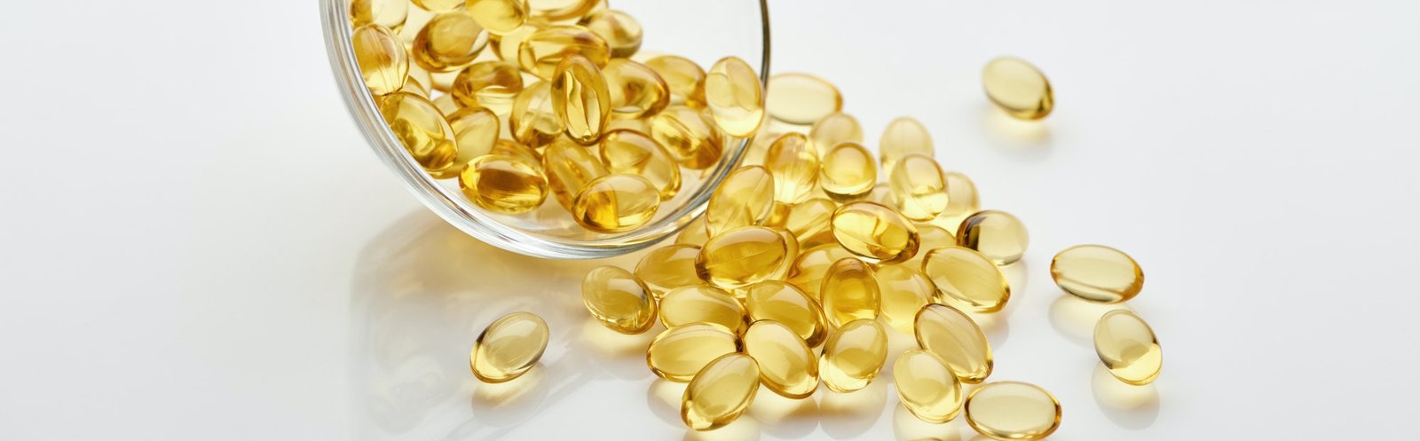 golden fish oil capsules in glass bowl on white background, panoramic shot