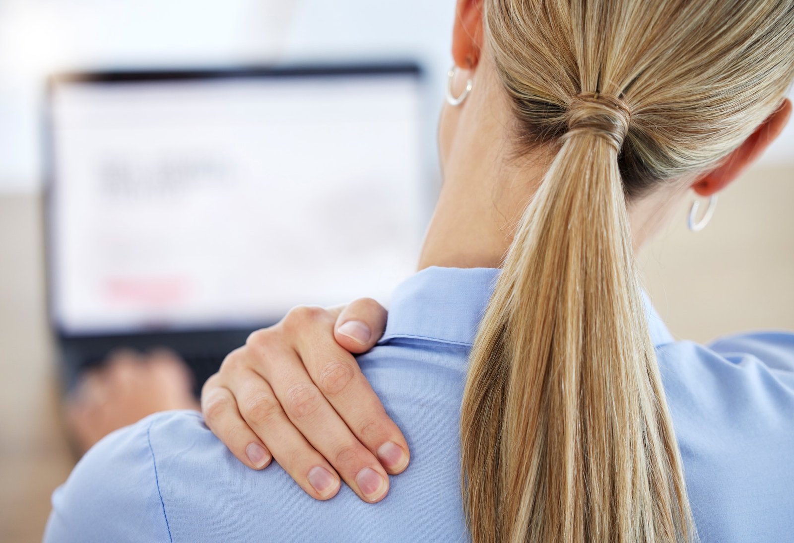Young business woman rubbing neck in pain while working in office from behind